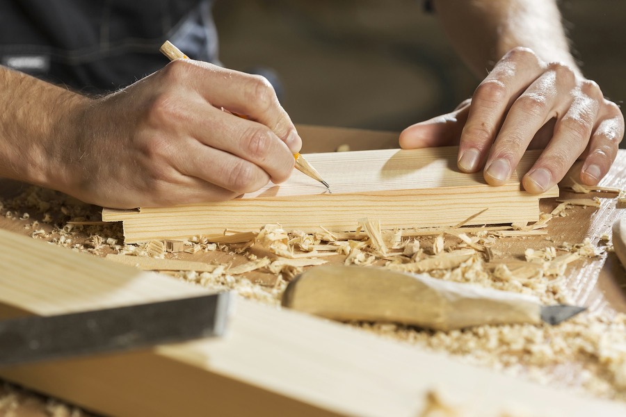 Hands marking the end of a timber section with a pencil.